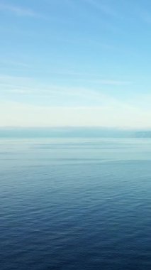 Açık mavi gökyüzünün altında, muhtemelen Fiumicello kıyı şeridi boyunca yumuşak dalgalarla sakin deniz manzarası. Huzurlu ve minimalist doğa sahnesi.