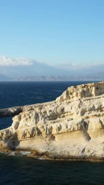 Yunanistan 'ın Girit kentindeki Matala kıyı şeridi boyunca uzanan derin mavi denize tepeden bakan kireçtaşı mağaralar ve engebeli uçurumlar. Açık gökyüzü ve uzak dağlar bu manzaralı Akdeniz manzarasını tamamlıyor.