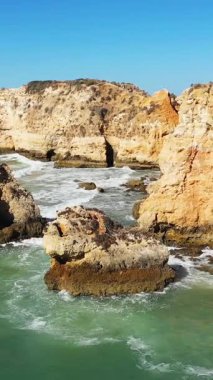Portekiz 'in Albufeira kıyısındaki Algarve kıyısında berrak mavi gökyüzünün altında dramatik altın kayalıklar ve kaya oluşumları turkuaz suların üzerinde yükseliyor..