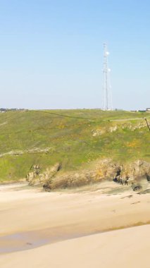 Kayalık kayalıkları olan geniş kumlu sahil ve açık mavi gökyüzünün altında Fransa 'nın Cap de Carteret kentindeki çimenli bir tepede uzun bir radyo kulesi..