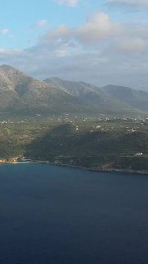 Yunanistan 'ın Mani bölgesinde, parçalı bulutlu bir gökyüzünün altında engebeli dağların ve Diros plajı yakınlarındaki kıyı şeridinin manzarası.