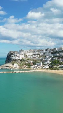 Beyazlatılmış Peschici kasabasının manzarası turkuaz suların üzerindeki bir uçuruma tünemiş ve İtalya 'da parçalı bulutlu bir gökyüzünün altında kumlu bir plaj..