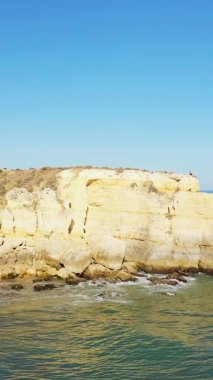 Berrak mavi gökyüzü ve Portekiz 'in Algarve şehrindeki sakin deniz kıyısında güneşli bir uçurum. Doğal kaya oluşumu okyanus suyunun üzerinde yükseliyor..