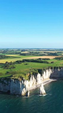 Etretat, Normandiya, Fransa 'daki ikonik beyaz tebeşir kayalıkları ve turkuaz denizin yeşil tarlaları ve açık mavi gökyüzü yaz mevsiminde görülmektedir..