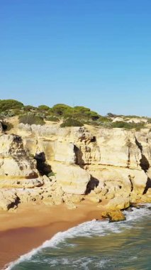 Portekiz 'in Albufeira yakınlarındaki Algarve bölgesinde dramatik uçurumları ve berrak mavi suları olan kumlu bir sahil manzarası. İnsanlar parlak, güneşli bir gökyüzünün altında kıyı şeridini severler..