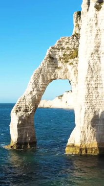 Fransa 'nın Etretat kıyı şeridi boyunca açık mavi bir gökyüzünün altında ünlü kireçtaşı kayalıkları ve doğal kemer oluşumunun manzarası.