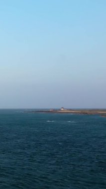 Fransa 'nın Normandiya kentinde açık mavi gökyüzü ve sakin denizin altında uzak bir deniz feneri bulunan Cap de la Hague kıyı şeridini geniş açıdan görebiliriz..