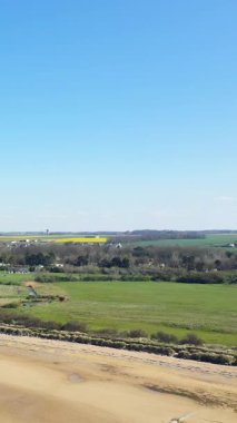 Bernieres-sur-Mer, Fransa 'daki Juno Sahili' nin geniş manzarası, açık mavi gökyüzü altında kumlu kumullar, çimenli kumullar ve kırsal.