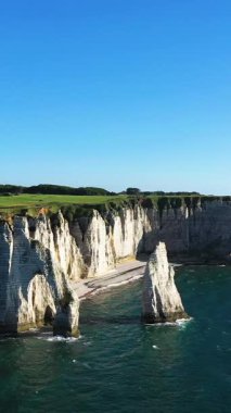 Fransa 'nın Normandiya kıyısındaki Etretat kıyı şeridi boyunca açık mavi gökyüzünün altında dramatik beyaz tebeşir kayalıkları ve deniz yığınları yükseliyor..