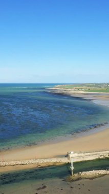Geniş bir kumsal manzarası ve açık mavi deniz Grandcamp-Maisy, Normandiya, Fransa 'da parlak bir gökyüzü altında. Yumuşak dalgalar ve kıyı manzaralı sakin kıyı şeridi.