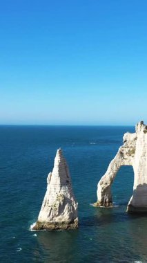 Etretat, Normandiya, Fransa 'da İngiliz Kanalı' nın mavi sularının üzerinde dramatik beyaz tebeşir kayalıkları ve doğal bir deniz kemeri yükseliyor. Açık gökyüzü ve sakin deniz sakin bir kıyı manzarası yaratır..