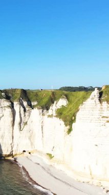 Açık mavi gökyüzünün altında yeşil çimlerle kaplı dramatik beyaz tebeşir kayalıkları, Etretat, Normandiya, Fransa.