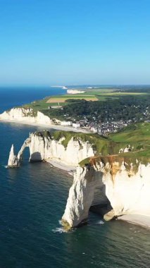 Etretat, Normandiya kıyı şeridi boyunca uzanan dramatik beyaz tebeşir kayalıklarının ve doğal kemerlerin havadan görünüşü ve arka planda yeşil alanlar..