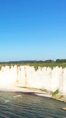 Mavi denizin üzerinde dramatik beyaz tebeşir kayalıkları yükseliyor ve açık bir gökyüzünün altında kumlu bir plaj Etretat, Normandiya, Fransa.