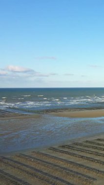 Fransa, Normandiya 'da Utah Sahili' nin kumlu sahillerinde, açık mavi bir gökyüzünün altında, arka planda hafif dalgalar olan istiridye yataklarının oluşturduğu sıra sıra..