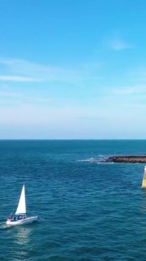 Beyaz bir yelkenli açık bir gökyüzünün altında Fransa 'nın Fecamp kentinin kayalık kıyı şeridine yakın mavi denizde süzülüyor. Canlı renklerle huzurlu bir deniz manzarası.