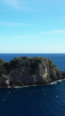 Açık bir gökyüzü altında açık mavi denizlere doğru yeşilliklerle kaplanmış dramatik kayalık kayalar, Capo di Conca, Amalfi Sahili, İtalya.