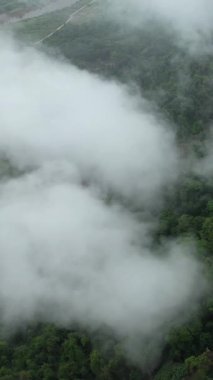 Kamboçya 'nın Phnom Penh yakınlarındaki yemyeşil kırsal arazinin insansız hava aracı görüntüsü alçak bulutlar ve sis bulutları yeryüzünün üzerinde sürükleniyor..