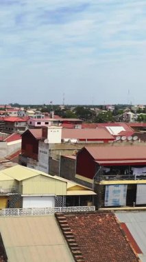 Elevated view of colorful rooftops and residential buildings in the city center of Battambang, Cambodia, under a partly cloudy sky.