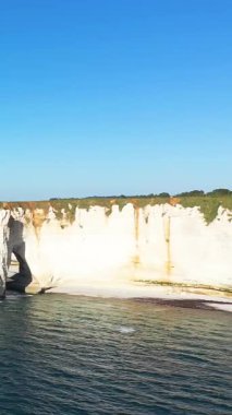 Etretat, Normandiya, Fransa 'da açık bir gökyüzü altında mavi denizin üzerinde dramatik beyaz tebeşir kayalıkları yükselir. Doğal kaya oluşumları ve durgun su içeren ikonik kıyı manzarası.