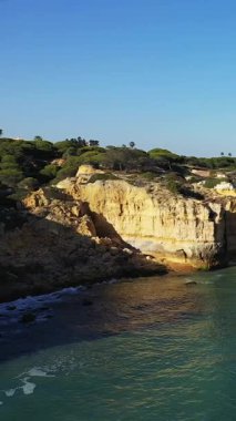 Portekiz 'in Albufeira kenti yakınlarındaki Algarve kıyısında berrak mavi gökyüzünün altında engebeli uçurumların ve berrak turkuaz suların manzarası..