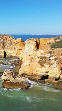 Portekiz 'in Albufeira yakınlarındaki Algarve kıyı şeridi boyunca dramatik kayalık kayalıklar ve berrak turkuaz suları parlak mavi bir gökyüzü altında..