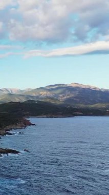 Korsika, Cargese yakınlarında bulutlu bir gökyüzünün altında berrak mavi denizi ve uzak dağları olan engebeli bir sahil manzarası. Doğal Akdeniz manzarası seyahat ve doğa kavramları için idealdir..