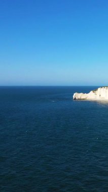 Etretat, Normandiya, Fransa 'da ikonik beyaz tebeşir kayalıkları ve açık bir gökyüzünün altında derin mavi deniz manzarası. Dramatik kıyı manzaralı sakin deniz manzarası.