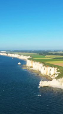 Etretat, Normandiya, Fransa kıyıları boyunca açık bir gökyüzü altında derin mavi denizle buluşan dramatik beyaz tebeşir kayalıklarının hava manzarası. Geniş tarım arazileri uçurumlar boyunca uzanır..
