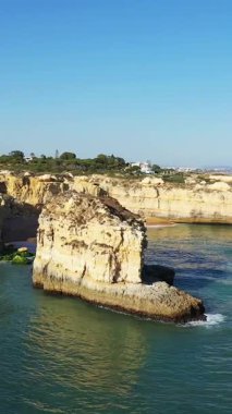 Portekiz 'in Albufeira yakınlarındaki Algarve kıyısında açık mavi gökyüzü ve durgun deniz ile dramatik kireçtaşı kayalıkları ve kaya oluşumları.