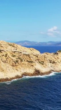 Parlak bir gökyüzünün altındaki derin mavi denize bakan antik bir taş kuleyle engebeli bir sahil manzarası. Fanale di Petra, Sardinya, İtalya yakınlarında yakalandı..