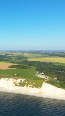 Etretat, Normandiya, Fransa kıyıları boyunca açık mavi bir gökyüzü altında ikonik beyaz tebeşir kayalıkları ve yemyeşil alanlar hava manzarası.