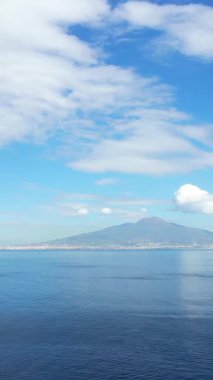 İtalya 'nın Napoli Körfezi' nde parçalı bulutlu bir gökyüzünün altındaki sakin mavi denizin manzarası. Uzak kıyı şeridi ve yumuşak ufuk huzurlu bir deniz manzarası yaratır..