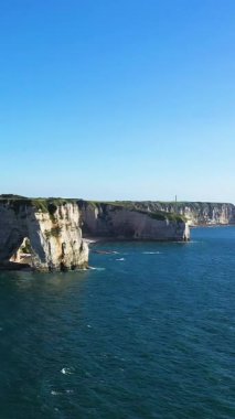 Etretat, Normandiya, Fransa 'da açık bir gökyüzü altında mavi denizin üzerinde dramatik beyaz tebeşir kayalıkları yükselir. Doğal kaya oluşumları ve sakin okyanusları olan manzaralı kıyı manzarası..