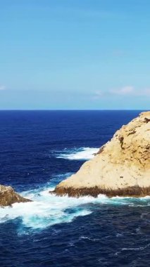 Açık mavi deniz dalgaları, parlak bir gökyüzünün altında, Fanale di Petra, Korsika 'daki kayalık kayalıklara çarpar. Seyahat ve doğa temaları için ideal Akdeniz kıyı manzarası.