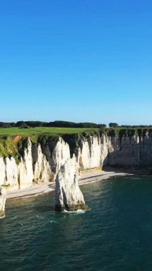 Fransa 'nın Normandiya kıyısındaki Etretat kıyısında açık bir gökyüzünün altında dramatik beyaz tebeşir kayalıkları yükseliyor. İkonik doğal kaya oluşumları ve yeşil alanlar çarpıcı bir manzara yaratır..
