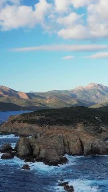 Kargese, Korsika yakınlarındaki mavi Akdeniz 'e bakan tarihi Ceneviz kulesine sahip dramatik kayalık kıyı şeridi. Arka planda parçalı bulutlu bir gökyüzünün altında dağlar var..