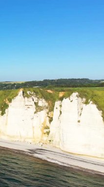 Etretat, Normandiya, Fransa 'da berrak mavi bir gökyüzünün altında ikonik beyaz tebeşir kayalıkları ve yeşil bir sahilin manzarası..