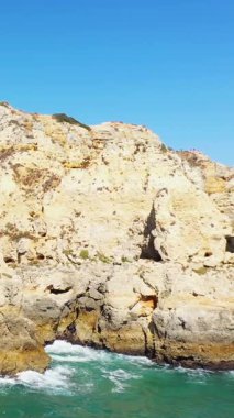 Portekiz 'in Lagos yakınlarındaki Algarve kıyısındaki turkuaz suların üzerinde açık mavi bir gökyüzünün altında dramatik altın uçurumlar yükseliyor..