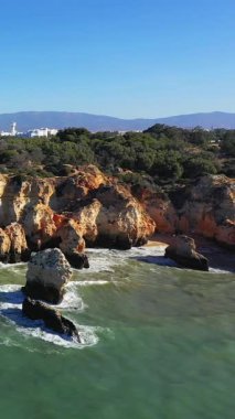 Portekiz, Albufeira yakınlarındaki Algarve kıyı şeridi boyunca parlak bir gökyüzünün altında dramatik kayalık kayalıklar ve berrak mavi sular..