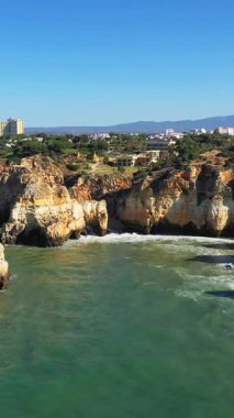 Portekiz 'in Albufeira kenti yakınlarındaki Algarve kıyısındaki engebeli uçurumlar ve turkuaz deniz manzarası berrak mavi bir gökyüzünün altında..