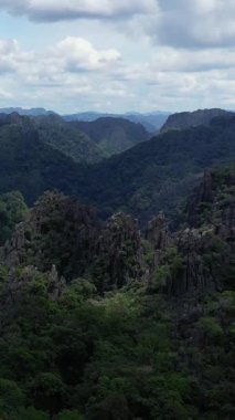 Laos kırsalında bulutlu bir gökyüzünün altında yoğun yeşil ormanlarla kaplı dramatik kireçtaşı zirveleri. Bu engebeli manzara Laos kırsalının doğal güzelliklerini gözler önüne seriyor..