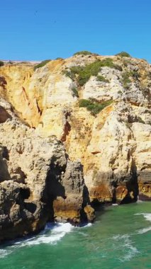 Portekiz 'in Lagos yakınlarındaki Algarve kıyısındaki turkuaz suların üzerinde açık mavi bir gökyüzünün altında dramatik altın uçurumlar yükseliyor..