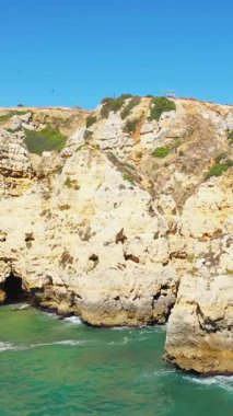 Portekiz 'in Lagos yakınlarındaki Algarve kıyısındaki berrak turkuaz suların üzerinde parlak mavi bir gökyüzünün altında dramatik kireçtaşı kayalıkları yükseliyor..
