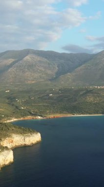 Yunanistan 'ın Mani Yarımadası' ndaki Diros Sahili yakınlarındaki engebeli kıyı şeridi ve dağların manzarası, parçalı bulutlu bir gökyüzü altında.