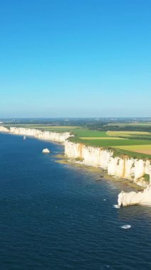 Etretat, Normandiya kıyı şeridi boyunca uzanan dramatik beyaz tebeşir uçurumlarının havadan görünüşü, açık bir gökyüzünün altında tarlalar ve mavi deniz. Sahne, Fransız sahilinin doğal güzelliğini ve çarpıcı manzarasını yakalıyor..