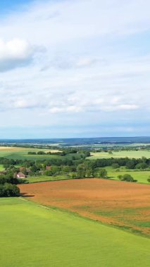 Bereketli yeşil tarlaların manzarası ve Nievre kırsalında küçük bir köy. Parlak mavi gökyüzünün altında dağınık bulutlar..