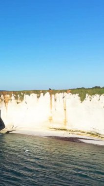 Etretat, Normandiya, Fransa 'da açık mavi gökyüzünün altında kumlu bir kumsal ve turkuaz deniz üzerinde dramatik beyaz tebeşir uçurumları yükselir. Doğal güzelliği ve dingin atmosferi olan ikonik kıyı manzarası.