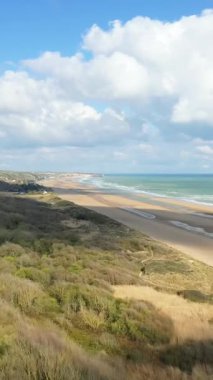 Fransa, Normandiya 'da parlak bir gökyüzü altında altın kum, yumuşak dalgalar ve dramatik bulutlarla geniş bir Omaha Sahili manzarası..