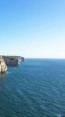Etretat, Normandiya, Fransa kıyıları boyunca açık bir gökyüzünün altında dramatik beyaz uçurumlar ve derin mavi deniz manzarası. Doğal manzara, engebeli uçurumların okyanusla buluştuğunu gösteriyor..